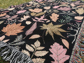 Close-up of rose gold and orange leaves on black autumn tapestry blanket